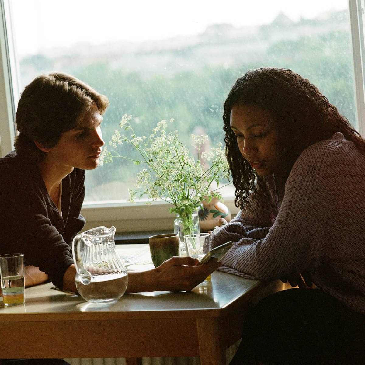 Två studenter sitter vid ett bord och visar något på mobilen