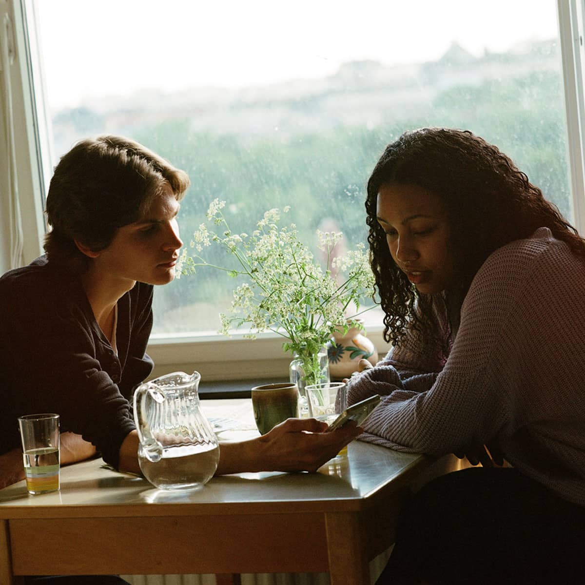 Två studenter sitter vid ett bord och visar något på mobilen