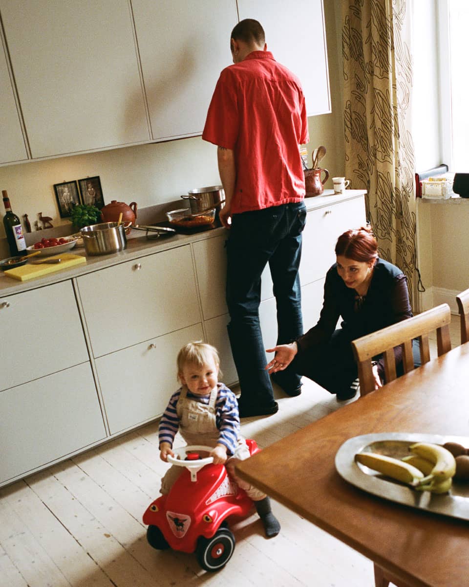 Ett barn åker på sparkbil i köket, med föräldrar i bakgrunden